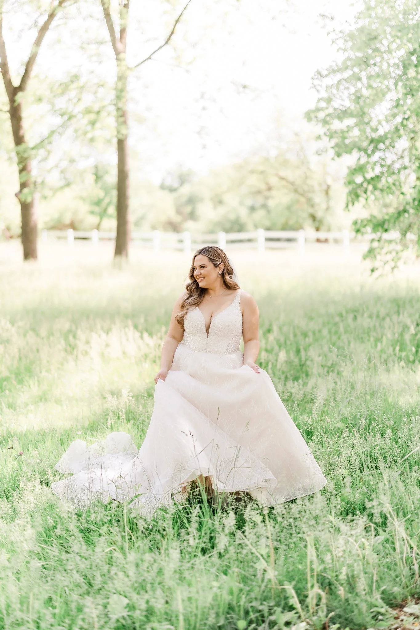 A bride in a white gown stands gracefully in a sunlit meadow.